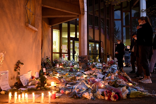 Des gens se tiennent devant des fleurs et des bougies à côté d'une affiche sur laquelle est écrit "Je suis un enseignant, je suis Samuel" à l'entrée d'un collège de Conflans-Sainte-Honorine, le 17 octobre 2020, après qu'un enseignant a été décapité par un agresseur abattu par des policiers. (Photo : BERTRAND GUAY/AFP via Getty Images)