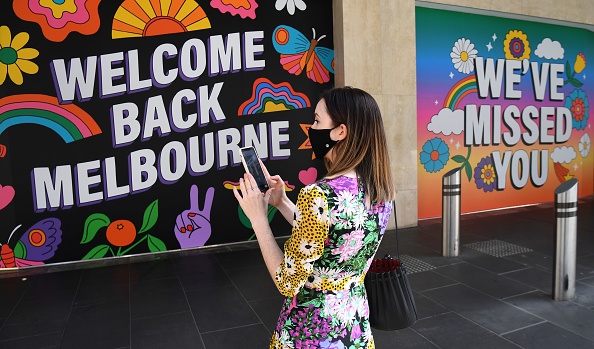 -Une femme se tient devant des affiches après que les mesures visant à freiner la propagation du coronavirus Covid-19 aient été atténuées, à Melbourne le 28 octobre 2020. Photo de William West / AFP via Getty Images.