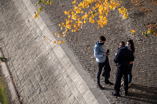 Un policier contrôle un couple sur les bords de la Seine, le 14 novembre 2020 à Paris (MARTIN BUREAU/AFP via Getty Images)