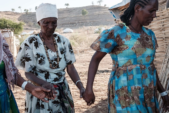 -L'Éthiopienne Asafu Alamaya, une aveugle de 80 ans qui a fui le conflit du Tigray, est guidée par sa fille dans le camp de réfugiés d'Um Raquba, le 12 décembre 2020. Photo par Yasuyoshi Chiba / AFP via Getty Images.