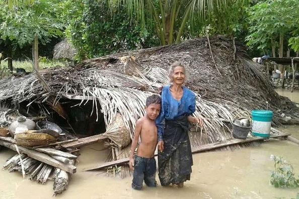 -Une villageoise âgée et son petit-fils dans les eaux de crue devant leur maison endommagée à East Flores le 4 avril 2021. Photo par Joy Christian / AFP via Getty Images.