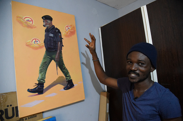 -Le peintre Julius Agbaje montre un tableau d'un policier à tête de chien, dans son studio au Lagos, le 25 mars 2021.  Photo Pius Utomi Ekpei /AFP via Getty Images.