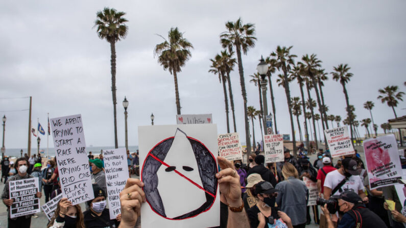 HUNTINGTON BEACH, CA - APRIL 11: Joe Cook Gines holds an anti-KKK playcard  during a protest against white supremacy at Huntington Beach Pier  on April 11, 2021 in Huntington Beach, California. The rally was organized by the Loyal White Knights and is believed to be part of a nationally coordinated group of white supremacist rallies in various cities across the nation. The Ku Klux Klan has been distributing flyers for the rally, and concerns in the Asian American and Pacific Islander communities are heightened as anti-Asian hate crimes have been rising since the start of the COVID-19 pandemic.(Photo by Apu Gomes/Getty Images)