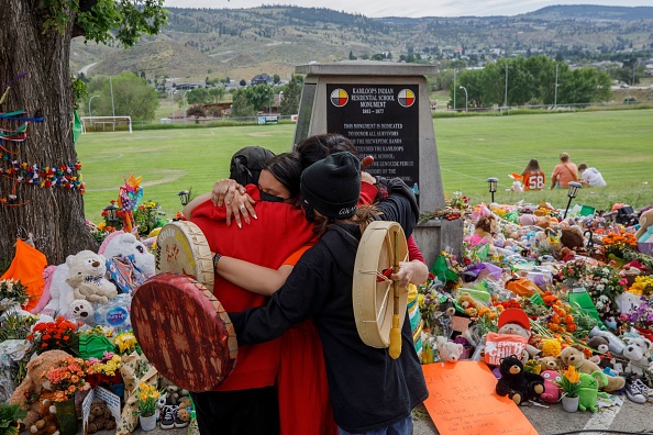 Membres de la Nation crie de Mosakahiken devant un mémorial de fortune érigé à l'ancien pensionnat indien de Kamloops en hommage aux 215 enfants dont les restes auraient été découverts enterrés près de l'établissement, à Kamloops, en Colombie-Britannique, au Canada, le 4 juin 2021. (Photo : COLE BURSTON/AFP via Getty Images)