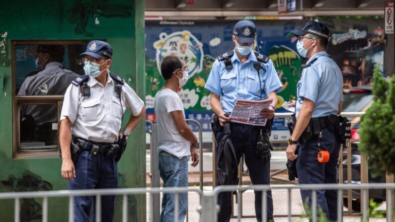 Un policier (au centre, à droite) lit un tract trouvé lors de l'interpellation et de la fouille d'un homme (2e à gauche) devant la Haute Cour de Hong Kong, le 30 juillet 2021, après que Tong Ying-kit a été condamné à neuf ans de prison pour terrorisme et incitation à la sécession lors du premier procès mené en vertu d'une loi sur la sécurité nationale imposée par la Chine. (Isaac Lawrence/AFP via Getty Images)