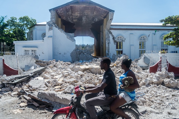 -Des gens passent devant les vestiges de l'église du "Sacré cœur des Cayes" aux Cayes le 15 août 2021. Photo de Reginald LOUISSAINT JR / AFP via Getty Images.