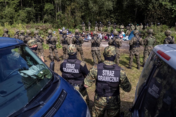 Des gardes-frontières polonais (au premier plan) se tiennent à côté de migrants supposés venir d'Afghanistan dans le petit village d'Usnarz Gorny près de Bialystok, dans le nord-est de la Pologne, situé près de la frontière avec le Bélarus, le 20 août 2021. (Photo : WOJTEK RADWANSKI/AFP via Getty Images)