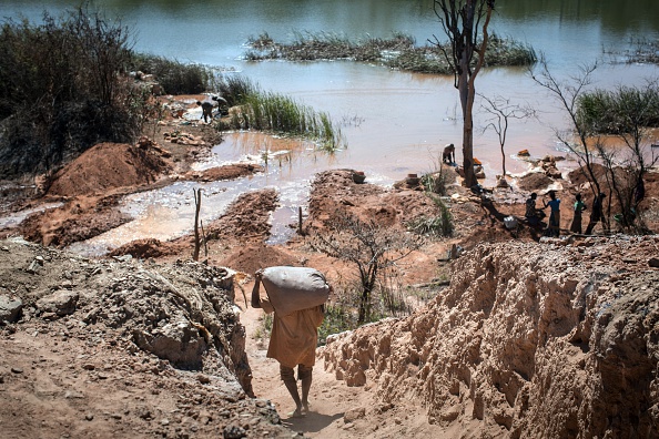 -Une mine en RDC un homme porte un sac de minéraux alors que des gens séparent le cobalt du sable et de la roche dans un lac de la région. Photo  FEDERICO SCOPPA/AFP via Getty Images.