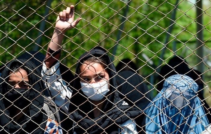 Une femme portant un masque regarde à travers un grillage. (WAKIL KOHSAR/AFP via Getty Images)