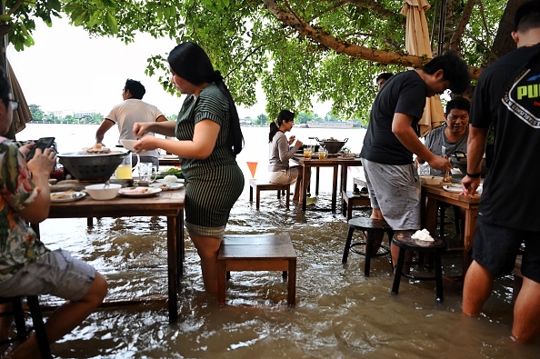 -Des gens debout savourent un dîner au Chaopraya Antique Café, alors que les eaux de crue de la rivière Chao Phraya déferlent dans le restaurant, au nord de Bangkok le 7 octobre 2021. Photo de Lillian SUWANRUMPHA / AFP via Getty Images