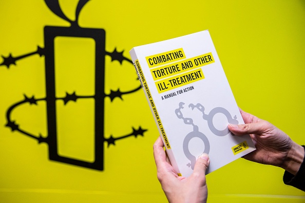 -Un employé d'Amnesty International tient une de leurs publications à côté de leur logo dans le bureau de Hong Kong en octobre 2021. Photo par Isaac LAWRENCE/AFP via Getty Images.