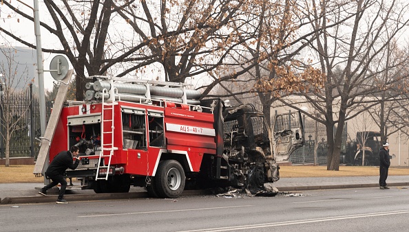 Un homme se protège derrière le véhicule d'un pompier incendié dans le centre d'Almaty le 7 janvier 2022. Photo d'ALEXANDR BOGDANOV / AFP via Getty Images.