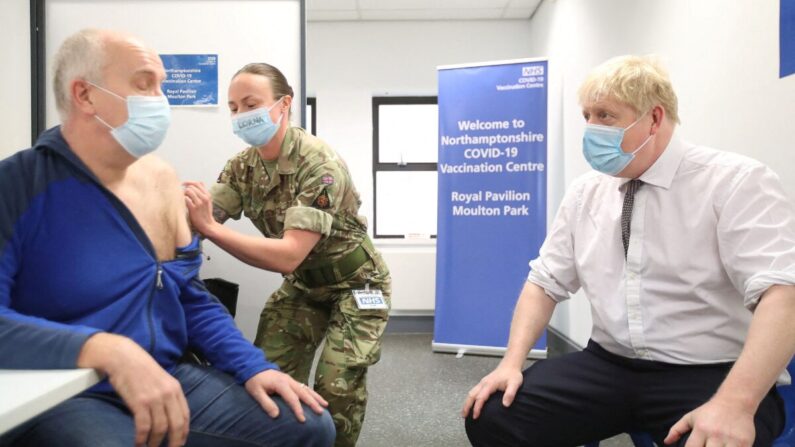 Le Premier ministre britannique Boris Johnson (à droite) est assis en face de Gordon Halfacre alors qu'il reçoit son vaccin Covid-19 de la caporale Lorna MacDonald lors d'une visite dans un centre de vaccination à Northampton, le 6 janvier 2022. (Peter Cziborra/Pool/AFP via Getty Images)