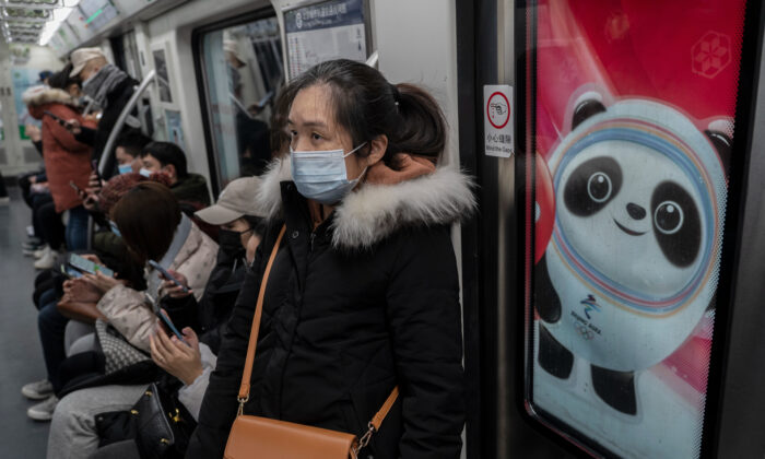 Une femme porte un masque de protection à côté d'un logo pour la mascotte des Jeux olympiques d'hiver de Pékin 2022, Bing Dwen Dwen, à l'heure de pointe à Pékin, en Chine, le 13 janvier 2022. (Kevin Frayer/Getty Images)