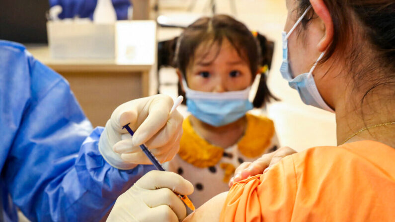 Une fillette regarde une femme qui se fait administrer le vaccin Covid-19 du groupe China National Biotec (CNBG) à Nantong, dans la province chinoise du Jiangsu (est), le 5 juillet 2021. (STR/AFP via Getty Images)