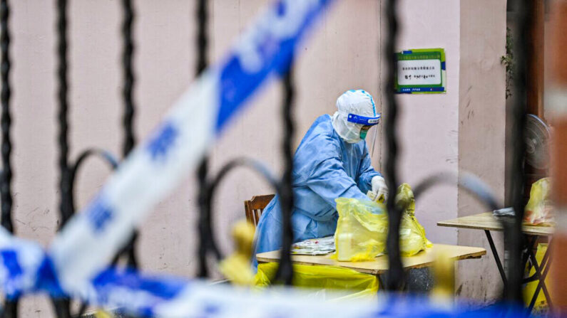 Un professionnel de la santé fouille dans un sac et des résidents sont soumis à un test de dépistage Covid-19 dans un complexe du district de Jing'an, à Shanghai, le 29 mars 2022. (Hector Retamal/AFP via Getty Images)