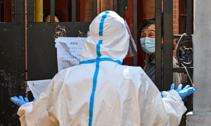 Un ouvrier, portant une tenue de protection, garde l'entrée d'un quartier en confinement, dans le district de Jing'an, à Shanghai, le 29 mars 2022. (Photo par HECTOR RETAMAL/AFP via Getty Images)