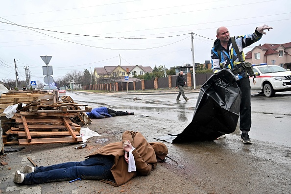 Le corps d'un civil avec les mains liées dans le dos gît dans la rue alors qu'un travailleur communal prépare un sac mortuaire en plastique pour le transporter, dans la ville de Bucha, non loin de la capitale ukrainienne de Kiev le 3 avril, 2022. Photo de Sergei SUPINSKY / AFP via Getty Images.