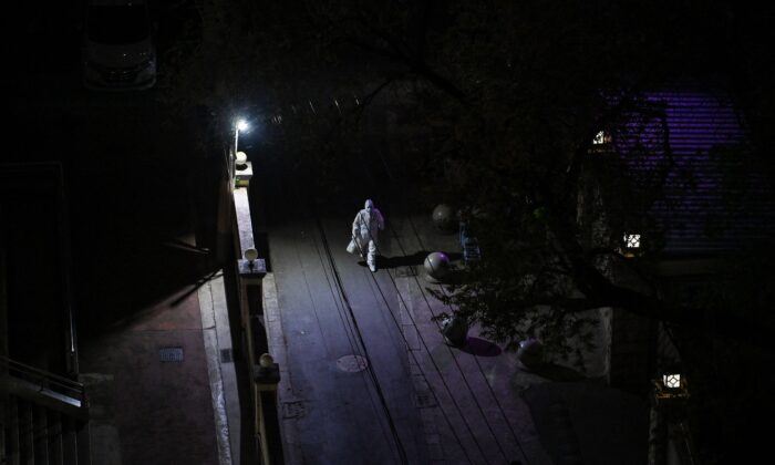 Un ouvrier, portant un équipement de protection individuelle (EPI), marche dans une rue la nuit pendant le confinement Covid-19 dans le quartier de Jing'an à Shanghai, le 10 avril 2022. (Photo par HECTOR RETAMAL/AFP via Getty Images)