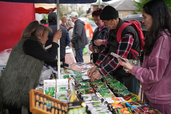 -Les résidents achètent des articles essentiels dans les étals de marché de fortune dans la ville de Bucha, qui commence à voir les services essentiels revenir le 15 mai 2022 à Bucha, en Ukraine. Photo de Christopher Furlong/Getty Images.