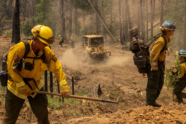 -Un bulldozer passe devant des pompiers coupant de la végétation pour élargir une ligne de feu à Oak Fire près de Mariposa, en Californie, le 25 juillet 2022. Photo de DAVID MCNEW/AFP via Getty Images.