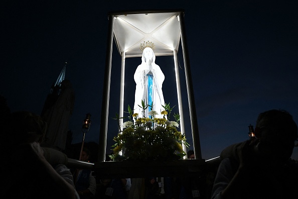 Des volontaires portent une réplique de la statue Cabuchet de la Vierge Marie lors de la procession mariale aux flambeaux à Lourdes, le 14 août 2022. Photo de Valentine CHAPUIS / AFP via Getty Images.