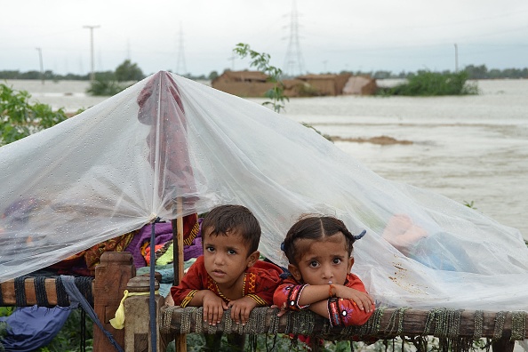 Des enfants s'abritent de la pluie sous une bâche en plastique dans un sol sec près de leur maison en terre effondrée dans une zone touchée par les inondations, dans la province du Balouchistan, le 25 août 2022. Photo de FIDA HUSSAIN/AFP via Getty Images.