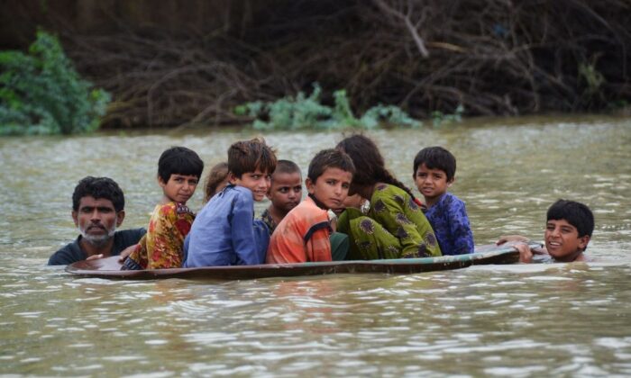 Deux hommes utilisent une antenne parabolique pour permettre aux enfants de traverser une zone inondée après de fortes pluies de mousson dans le district de Jaffarabad, province du Baloutchistan, Pakistan, le 26 août 2022. (Fida Hussain/AFP via Getty Images)