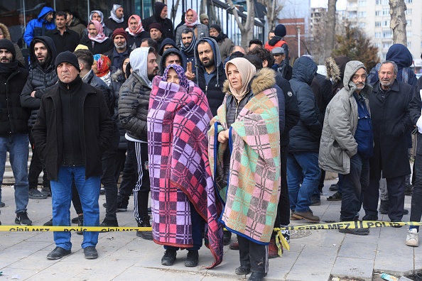 Des femmes se couvrent de couvertures parmi les spectateurs alors que les sauveteurs recherchent des victimes et des survivants dans les décombres de bâtiments effondrés à Gaziantep. (ZEIN AL RIFAI/AFP via Getty Images)