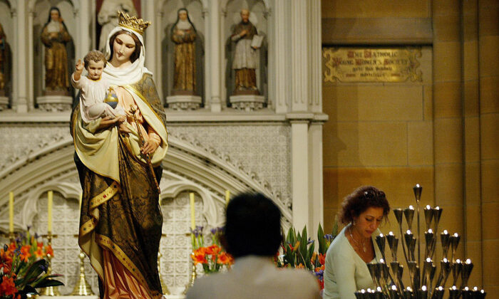 Un fidèle allume une bougie tandis qu'un autre prie à l'intérieur de la cathédrale St Mary à Sydney, en Australie, le 1er avril 2005. (Rob Elliot/AFP via Getty Images)