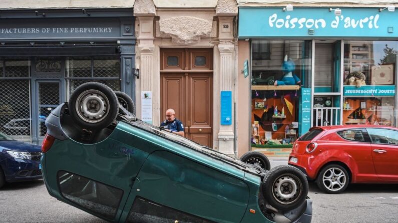 Un policier municipal dresse un PV au véhicule de Julie Lopes alors qu'il a été pris pour cible par les émeutiers et renversé dans la rue. (Crédit photo  OLIVIER CHASSIGNOLE / AFP)