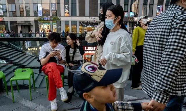 Le 18 avril 2023, un couple regarde un téléphone portable en attendant une table à l'extérieur d'un restaurant dans une zone commerciale de Pékin, en Chine. (Kevin Frayer/Getty Images)