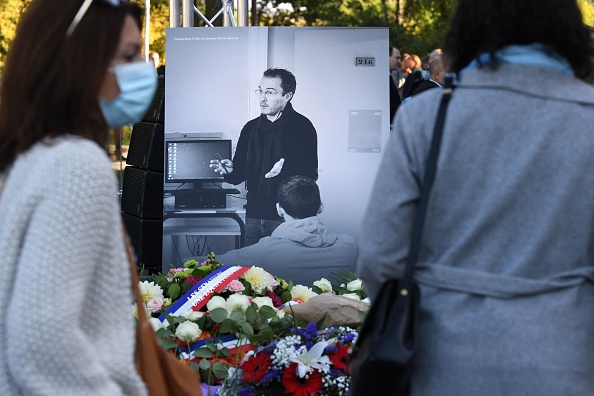 Des membres du public se tiennent devant une photo représentant le professeur d'histoire et de géographie Samuel Paty lors d'une cérémonie d'hommage à Éragny-sur-Oise. (Photo ALAIN JOCARD/AFP via Getty Images)