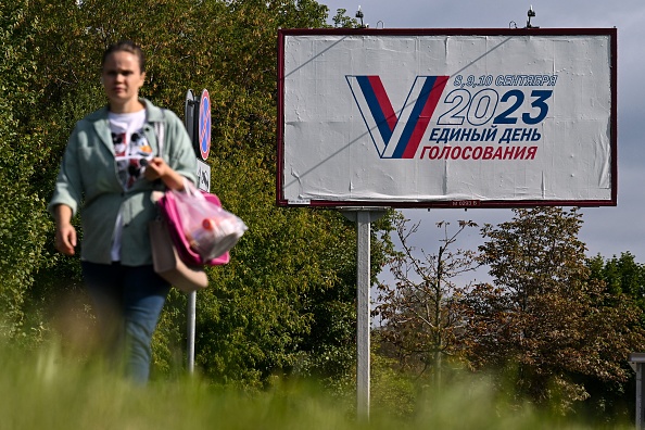 Une femme marche devant un panneau d'affichage annonçant les prochaines élections locales de trois jours en Russie et dans les régions de l'Ukraine contrôlées par la Russie. (Photo NATALIA KOLESNIKOVA/AFP via Getty Images)