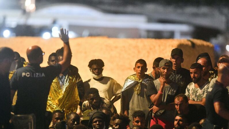 Un agent de police italien (à g.) en face de migrants, sur l'île italienne de Lampedusa, le 13 septembre 2023. (Photo ALESSANDRO SERRANO/AFP via Getty Images)