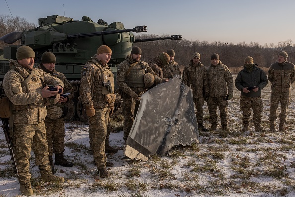 Des militaires ukrainiens d'une équipe de chasseurs de drones et un drone russe peint en noir qui aurait été abattu, à côté d'un char antiaérien allemand Gepard, dans la banlieue de Kiev, le 30 novembre 2023. (Photo ROMAN PILIPEY/AFP via Getty Images)