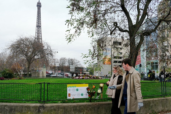 Des piétons passent devant des fleurs à l'endroit où un touriste a été poignardé à mort la veille, près de la Tour Eiffel (en arrière-plan), à Paris, le 3 décembre 2023. (Photo DIMITAR DILKOFF/AFP via Getty Images)