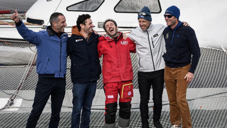 Armel Le Cleac'h, Anthony Marchand, Eric Peron, Thomas Coville et Charles Caudrelier posent sur le multicoque Adagio après la cinquième place d'Eric Peron dans la course à la voile en multicoque autour du monde en solitaire Arkea Ultim Challenge, à Brest, le 13 mars 2024. (Photo : LOIC VENANCE/AFP via Getty Images)