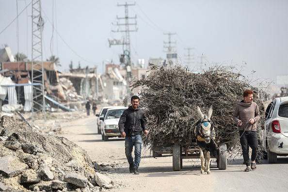 Des Palestiniens conduisent une charrette tirée par un âne devant les ruines des bâtiments dans la bande de Gaza, le 27 février 2024. (Photo AFP via Getty Images)