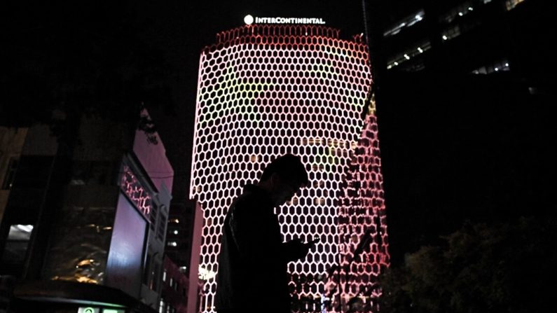 Un homme regarde son téléphone près d'une image géante du drapeau du PCC sur le côté d'un bâtiment à Pékin, pendant le 19e Congrès du Parti communiste, le 23 octobre 2017. (GREG BAKER/AFP via Getty Images)