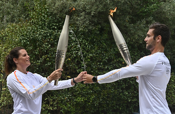 Le premier porteur de la torche, Stefanos Ntouskos, médaillé d'or olympique en aviron en 2020, allume la torche tenue par la deuxième porteuse, la nageuse olympique Laure Manaudou. (Photo VALERIE GACHE/AFP via Getty Images)