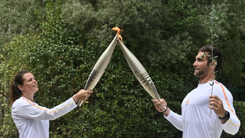 Le premier porteur de la torche, Stefanos Ntouskos (à dr.), médaillé d'or olympique en aviron en 2020, allume la torche tenue par Laure Manaudou (à g.), deuxième nageuse olympique française, le 16 avril 2024, en Grèce. (Photo VALERIE GACHE/AFP via Getty Images)