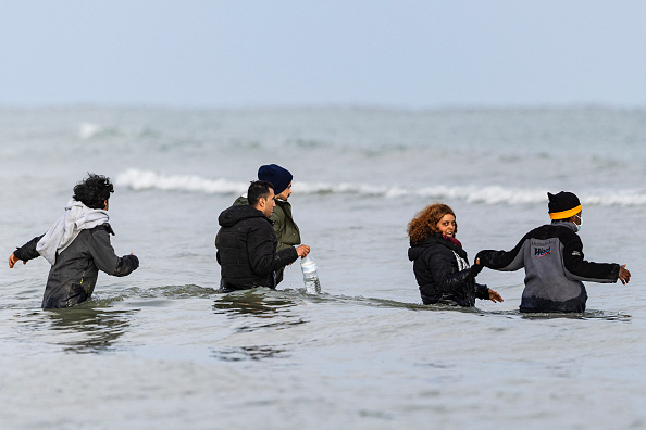 Des migrants marchent dans la mer pour monter à bord d'un bateau de passeurs afin de tenter de traverser la Manche, sur la plage de Gravelines près de Dunkerque, le 26 avril 2024. (SAMEER AL-DOUMY/AFP via Getty Images)