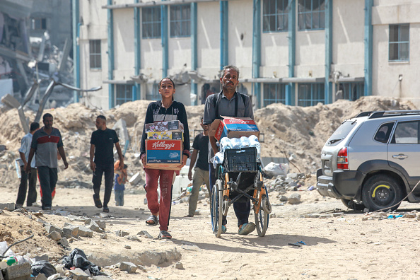 Des Palestiniens marchent avec de l'eau et de l'aide alimentaire dans un quartier résidentiel très endommagé de la ville de Khan Yunis. (BASHAR TALEB/AFP via Getty Images)