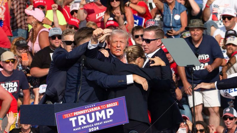 Le candidat républicain Donald Trump apparaît avec ce qui semble être du sang sur son visage, entouré d'agents des services secrets, alors qu'il est évacué de la scène lors d'un événement de campagne à Butler Farm Show Inc. à Butler, en Pennsylvanie, le 13 juillet 2024. (REBECCA DROKE/AFP via Getty Images)