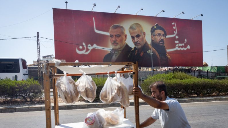 Un homme pousse son chariot de nourriture devant un panneau d'affichage montrant le chef du Hamas décédé, Ismail Haniyeh, le général Qasem Soleimani, qui a servi dans la Garde révolutionnaire iranienne, et le commandant en chef du Hezbollah, Fuad Shukr, à Beyrouth, au Liban, le 6 août 2024. (Chris McGrath/Getty Images)