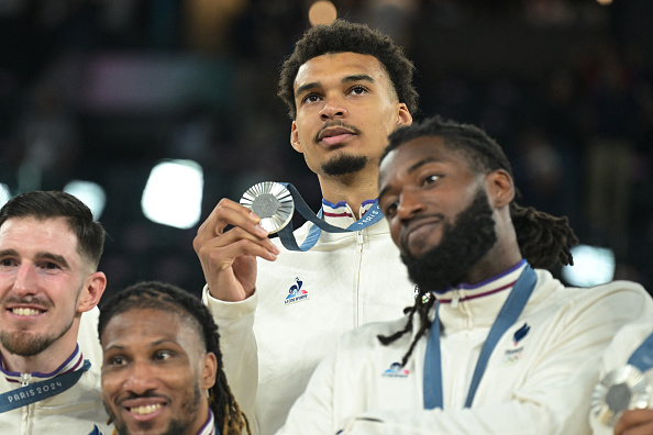 Nando De Colo, Andrew Albicy, Victor Wembanyama et Mathias Lessort sur le podium le 10 août 2024. (Photo DAMIEN MEYER/AFP via Getty Images)