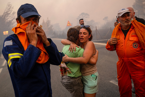 Deux femmes secourues lors d'un incendie de forêt à Varnavas, au nord d'Athènes, le 11 août 2024. (Photo ANGELOS TZORTZINIS/AFP via Getty Images)