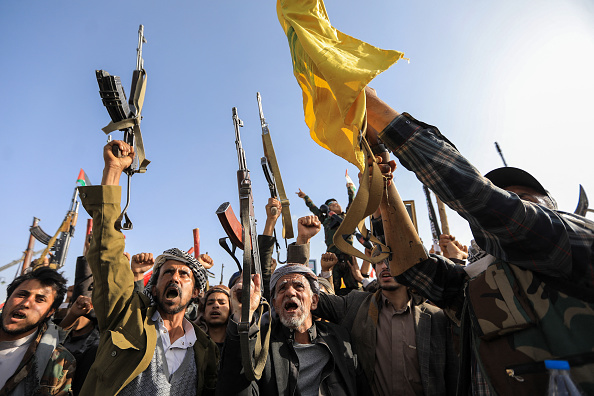 Des terroristes houthis lèvent leurs fusils automatiques en l'air avec un drapeau jaune du mouvement Hezbollah libanais lors d'un rassemblement organisé à Sanaa le 27 septembre 2024 pour protester contre les attaques d'Israël au Liban et à Gaza. (Photo ABDALLAH ADEL/AFP via Getty Images)