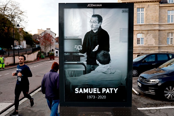 Des piétons passent devant une affiche représentant l'enseignant Samuel Paty placée dans le centre-ville de Conflans-Sainte-Honorine. (THOMAS COEX/AFP via Getty Images)